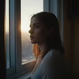 young woman looks out of window with view of city