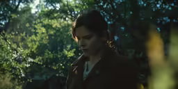 a woman in a brown coat looks down at her cellphone