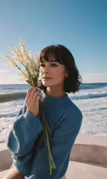 a woman holding a bouquet of flowers sitting on the beach