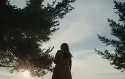 a girl standing in front of some trees and a sun