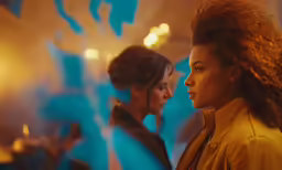 two young women look out a window at one another