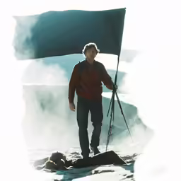 a man in brown sweater holding a flag over the top of a mountain