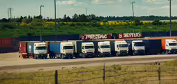 large semi trucks sit in a line along a road,eighteen wheeler trucks lined up next to each other