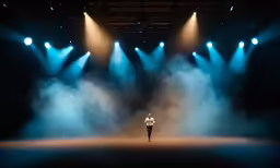a man stands on the stage in front of three blue light spotlights