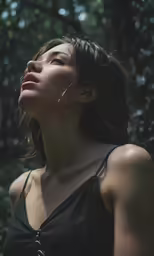 a woman is staring upward while standing in a wooded area