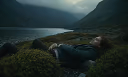 there is a man laying on a rock next to the water