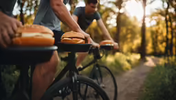 two cyclists riding bicycles in the woods while eating burgers