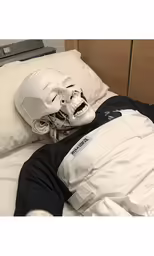 a helmeted man lays in bed with his head tucked between the sheets