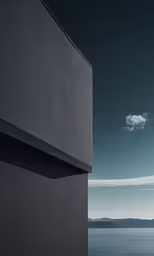 a black building stands by the ocean with mountains and clouds
