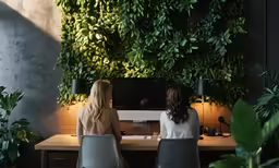 two women are sitting in chairs talking at a desk