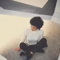 woman sitting on concrete with open arms, wearing black pants and a sweater