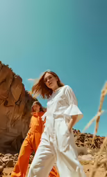 two women in orange pants and white jumpsuits in the desert