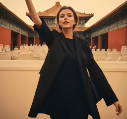 a woman with her hand up standing in front of a building