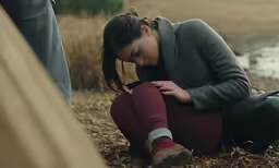 a woman is sitting by the river, her head down