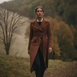 a woman in brown coat and black pants standing on road