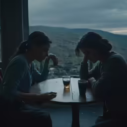 two woman are sitting at a wooden table