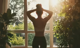 a woman in her underwear stands and looks out the window at the countryside