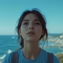 woman staring up while standing in front of a sea and rocks