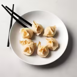 four asian dumplings on a plate with black chopsticks