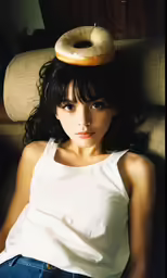 a girl sits in a chair with a donut on her head