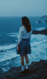 a girl is staring out at the water on the shore