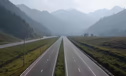 two lanes of road with trees and mountains in the distance