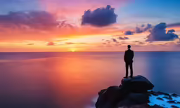 man standing on a cliff looking at the sun setting over the ocean