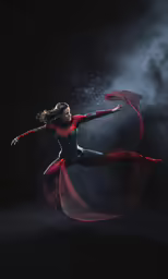 a woman in a red and blue jumpsuit with her arms outstretched as she stretches through the air in a swirling veil