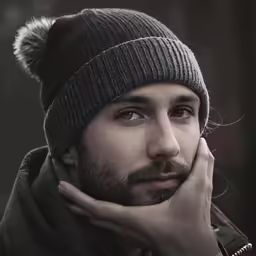 a man with a furry pom hat on is leaning his head to the side