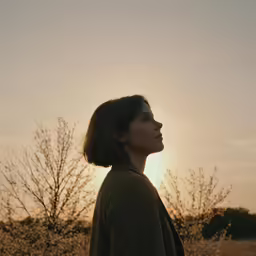 a young woman standing in front of a sunset