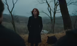 the woman in a dark coat is standing near a black cat