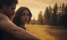 a young man holds the arm of a woman in front of an out of focus sun