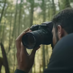 a man holding a camera with trees in the background