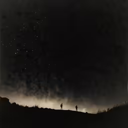 two people are standing in the middle of a field at night under stars