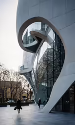 people walk past a futuristic building in the winter