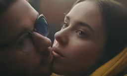 a woman wearing glasses kissing a man who is wearing a scarf