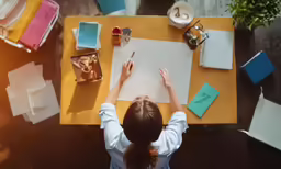 a woman sitting at a table drawing with markers