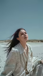 a woman in a white coat sitting on a sandy beach