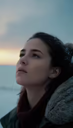a girl stands near the water, and stares in the distance