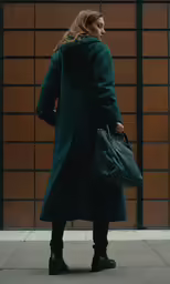 a woman wearing a long coat with a handbag and boots