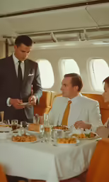 a waiter serving a meal to a couple in a airplane