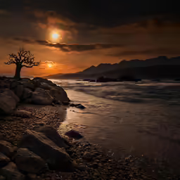 an ocean and rocks with the sun in background