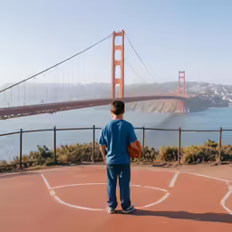 a person stands with a basketball in the middle of a basketball court near the golden gate bridge