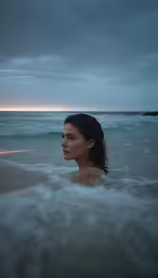 a woman in a wet bikini wading out to the ocean at sunset