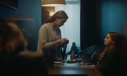 three people sitting at a table, one is using a phone