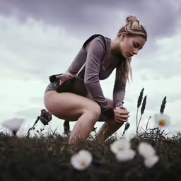 the woman is kneeling down to smell the grass