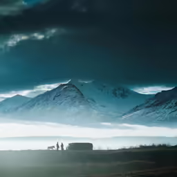 two people standing in the distance with snow covered mountains in the background