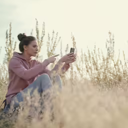 a woman sitting on a field using her phone