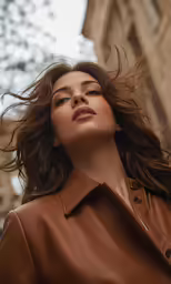 a beautiful young woman wearing a brown leather jacket with her hair blowing in the wind