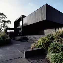two story building surrounded by plants and a stone path